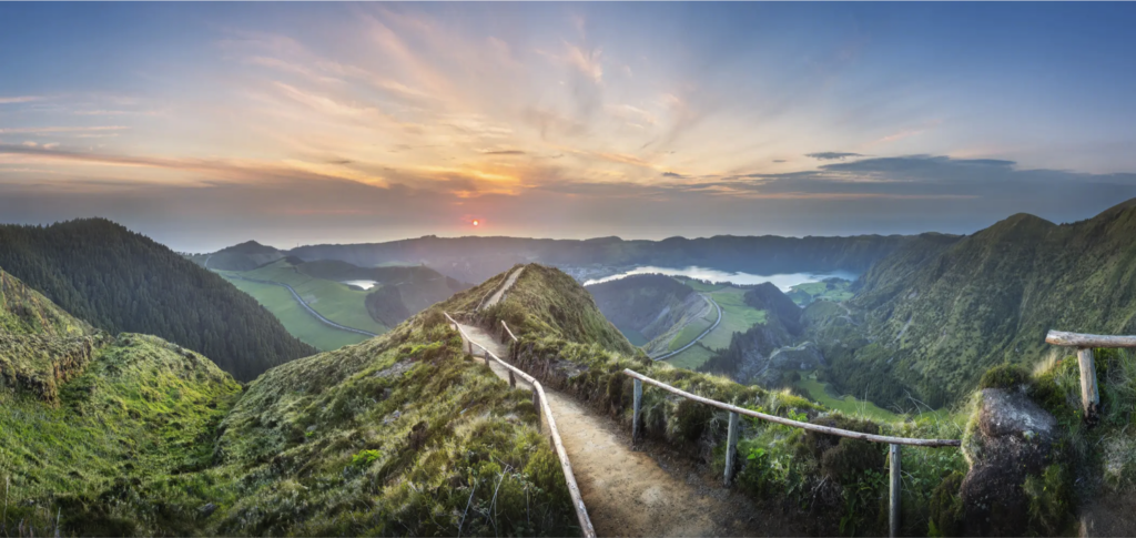 photo d'un sentier en haut d'une montagne, vue sur un coucher de soleil en 2e plan