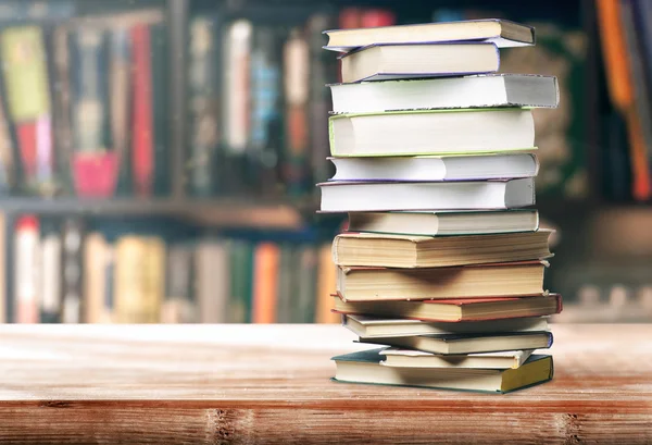 Photo d'une pile de livres sur un bureau avec une bibliothèque en fond